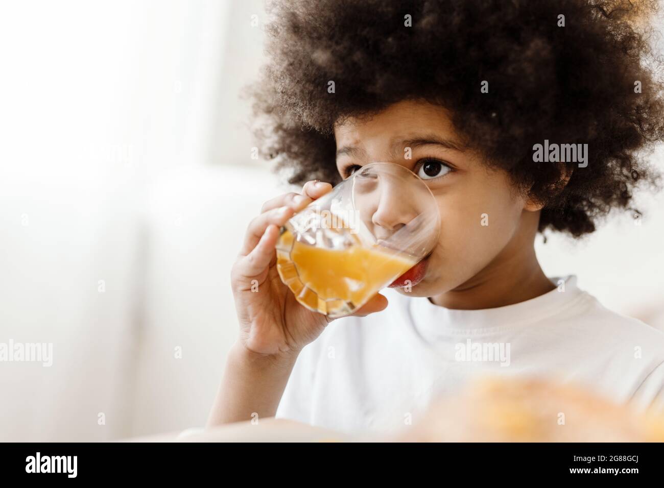 Black curly boy looking forward while drinking juice indoors Stock