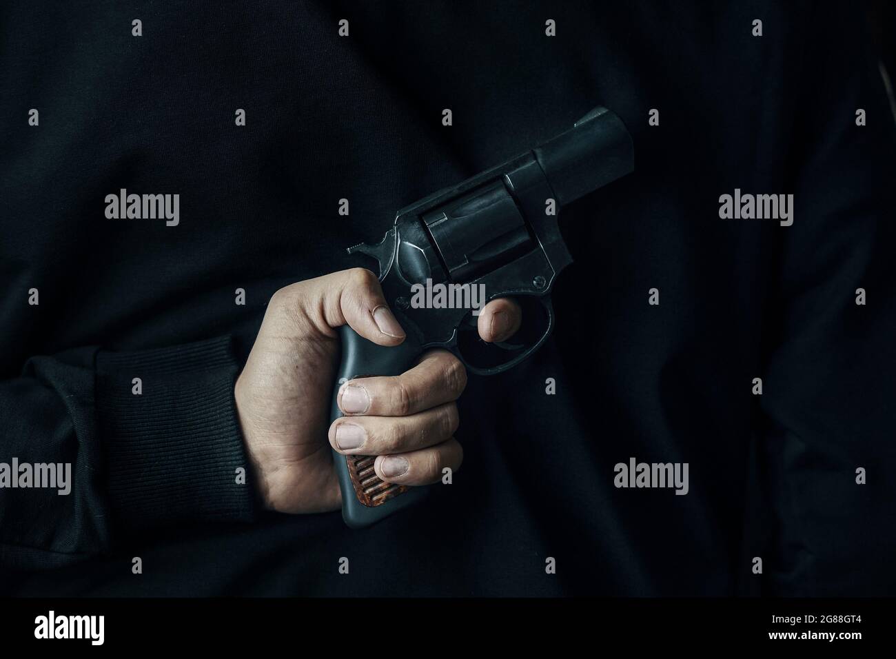 Man holds firearm behind his back. Person ready to attack with hand gun. Revolver in men's hand. Criminal concept. Stock Photo