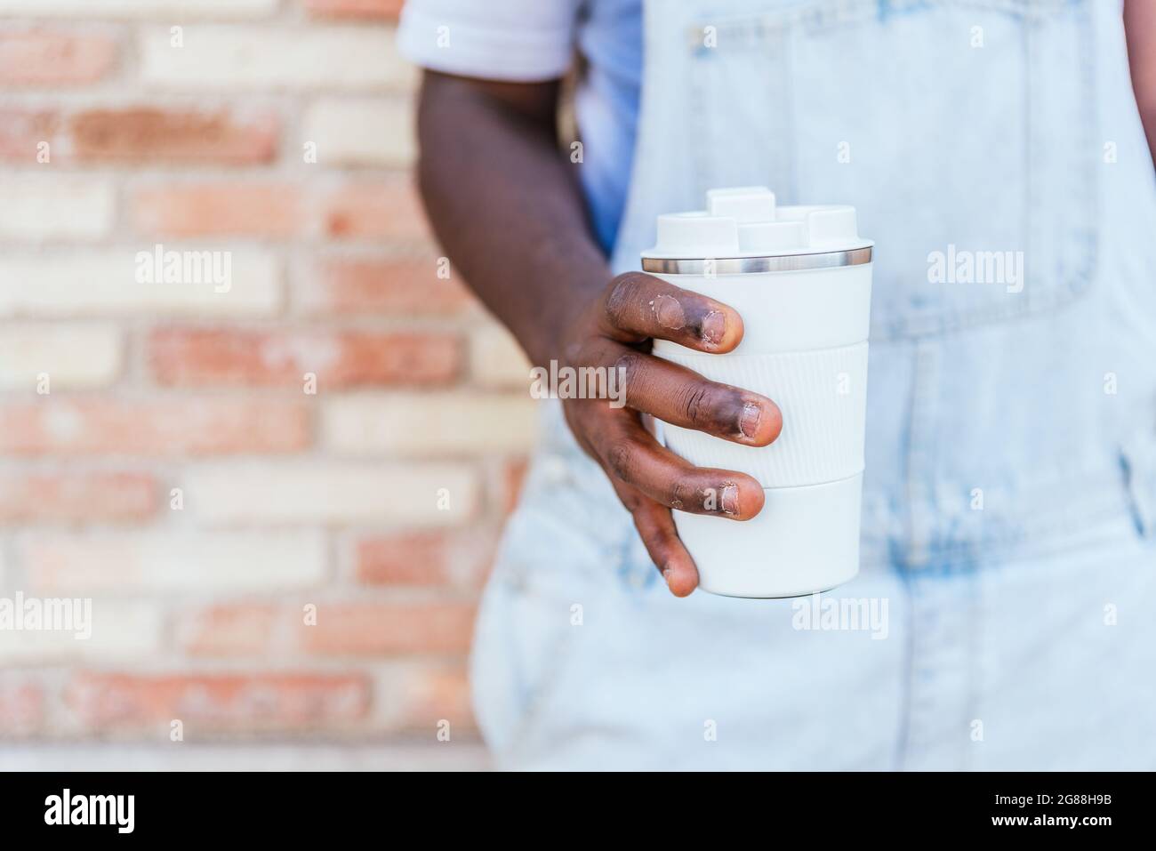 hands of an unrecognizable afro man holding a reusable cup of coffee. He has deteriorated skin Stock Photo