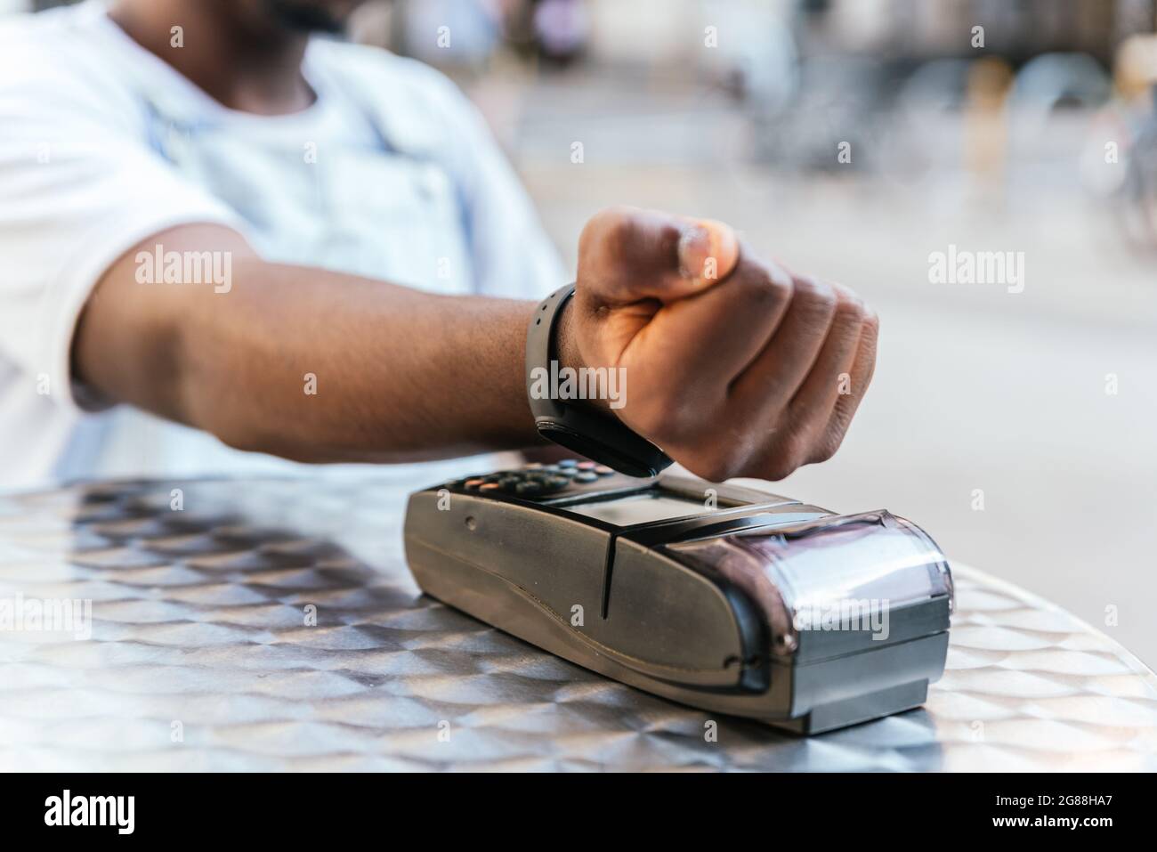 close up take of the hands of an unrecognizable afro american man paying with his watch. He is sitting on a chair on a bar terrace Stock Photo