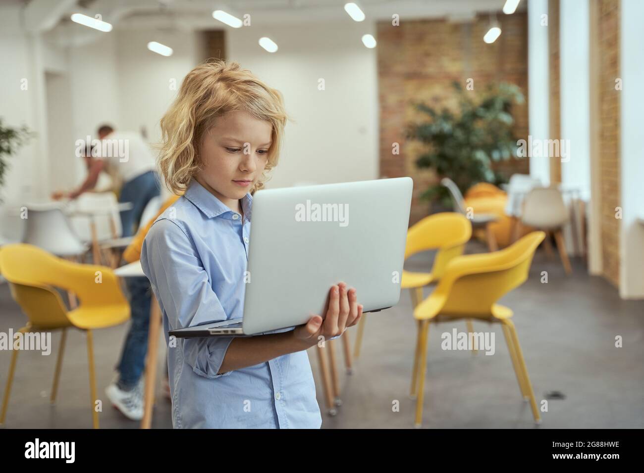 Portrait of busy little boy holding and using laptop while posing in a ...