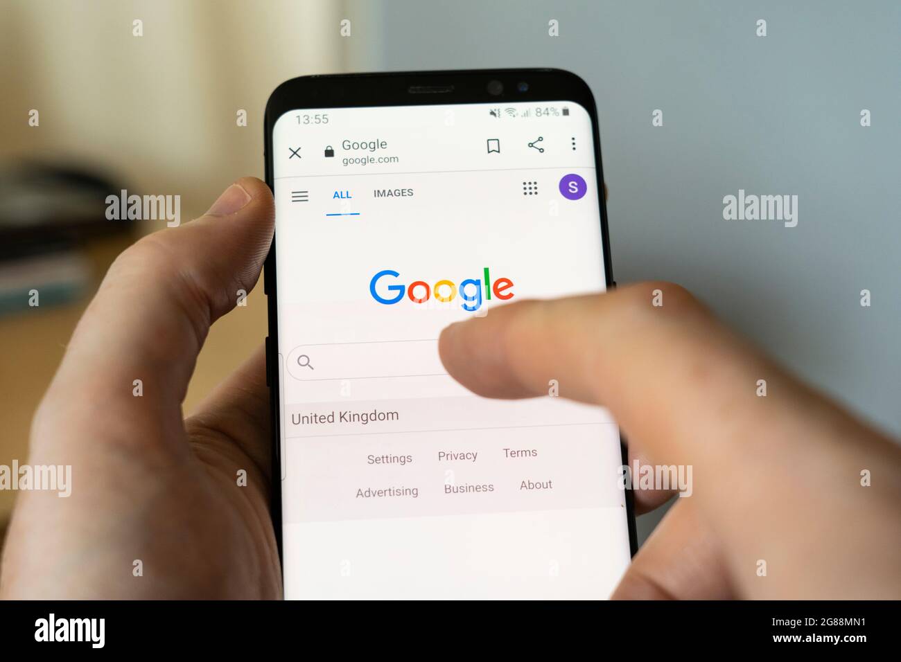 A man's hand holding an Android smartphone at home and selecting the Google Search bar on the google.com search engine homepage Stock Photo
