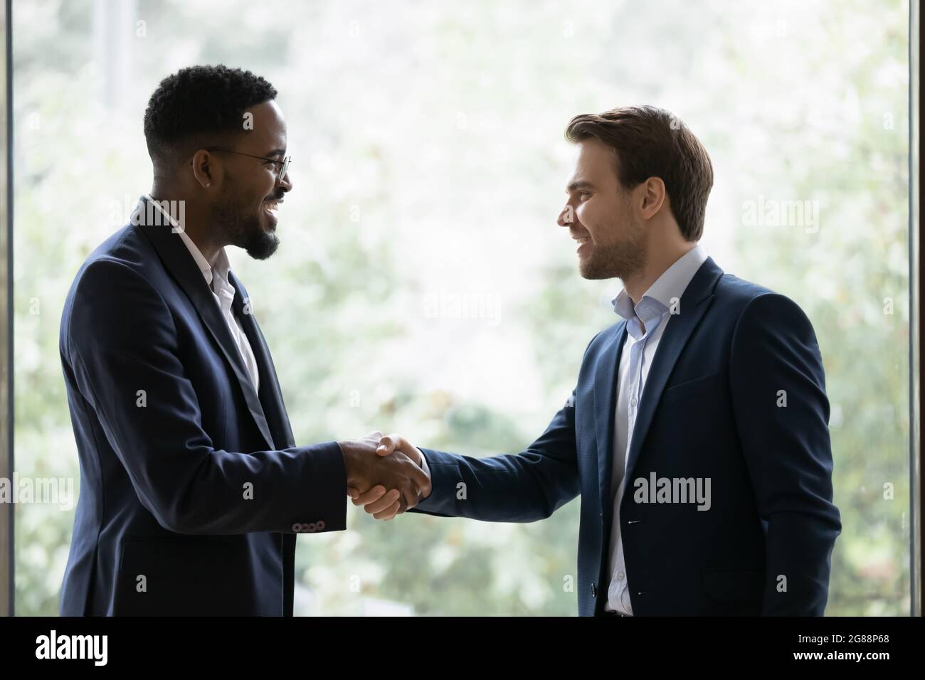 Two diverse businessmen, business partners shaking hands at window Stock Photo