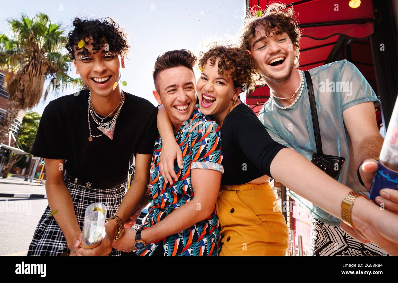 Carefree friends celebrating with confetti outdoors. Group of happy queer people smiling cheerfully while celebrating their friendship. Friends bondin Stock Photo