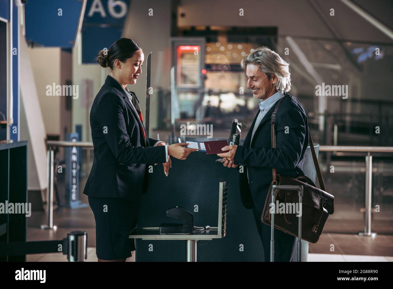 Businessman getting his boarding pass scanned at check in counter. Female ground attendant giving boarding pass and passport to male traveler. Stock Photo