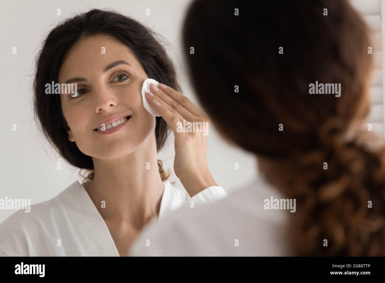 Young hispanic female remove makeup by mirror using sponge Stock Photo