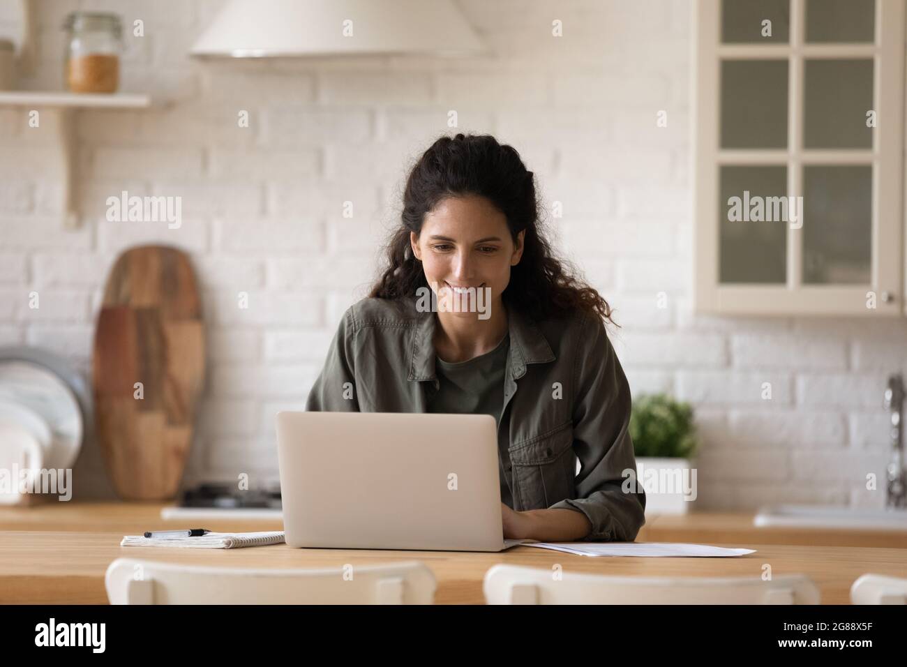 Busy latin lady writing business email on laptop at kitchen Stock Photo