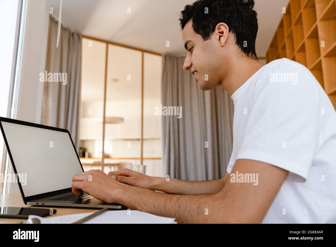 Pensive young hispanic man working studying on laptop computer while sitting at the desk at home Stock Photo