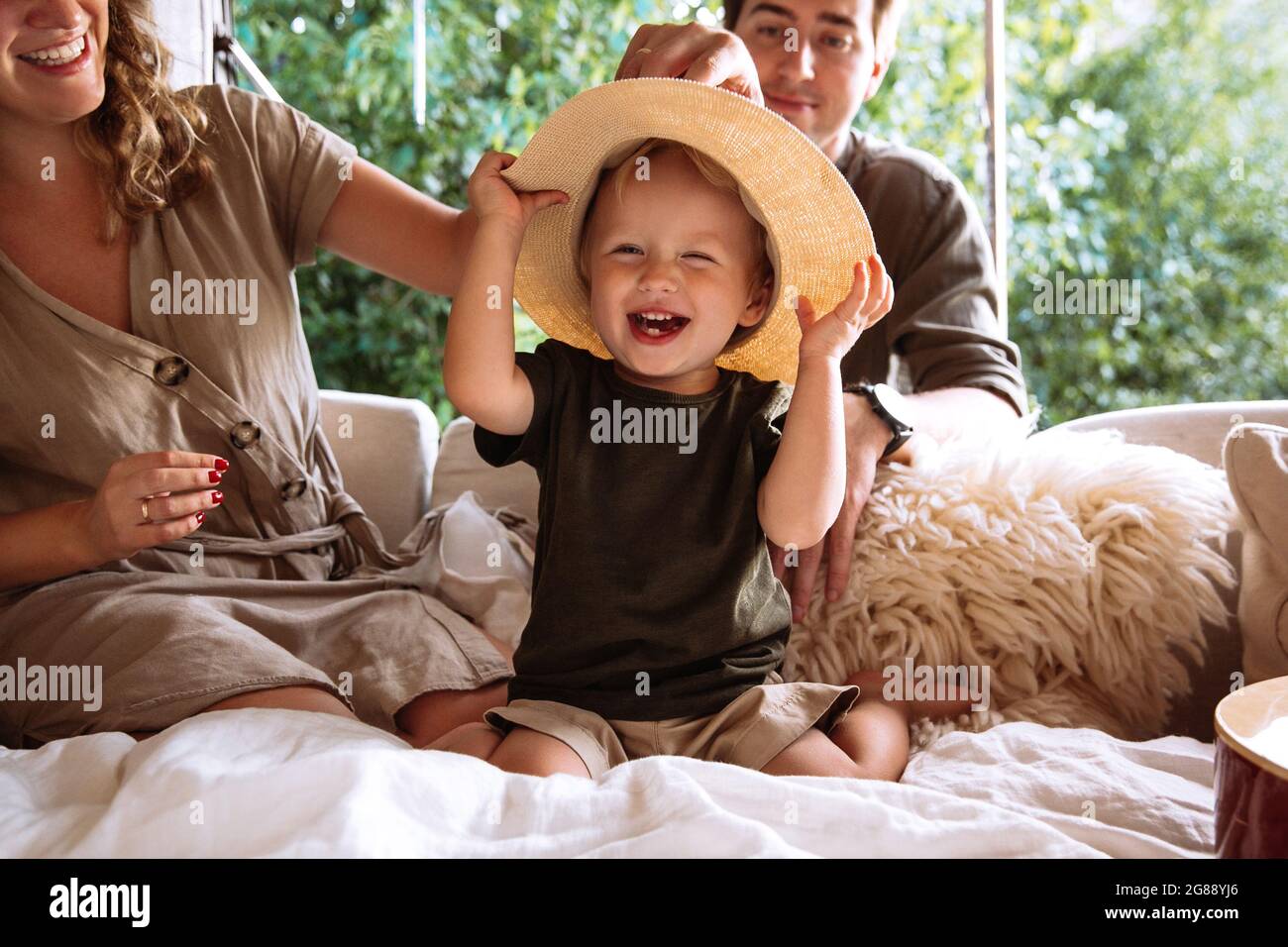 Portrait of cute small boy in straw hat with parents in cozy bedroom rv with window in summer forest Stock Photo