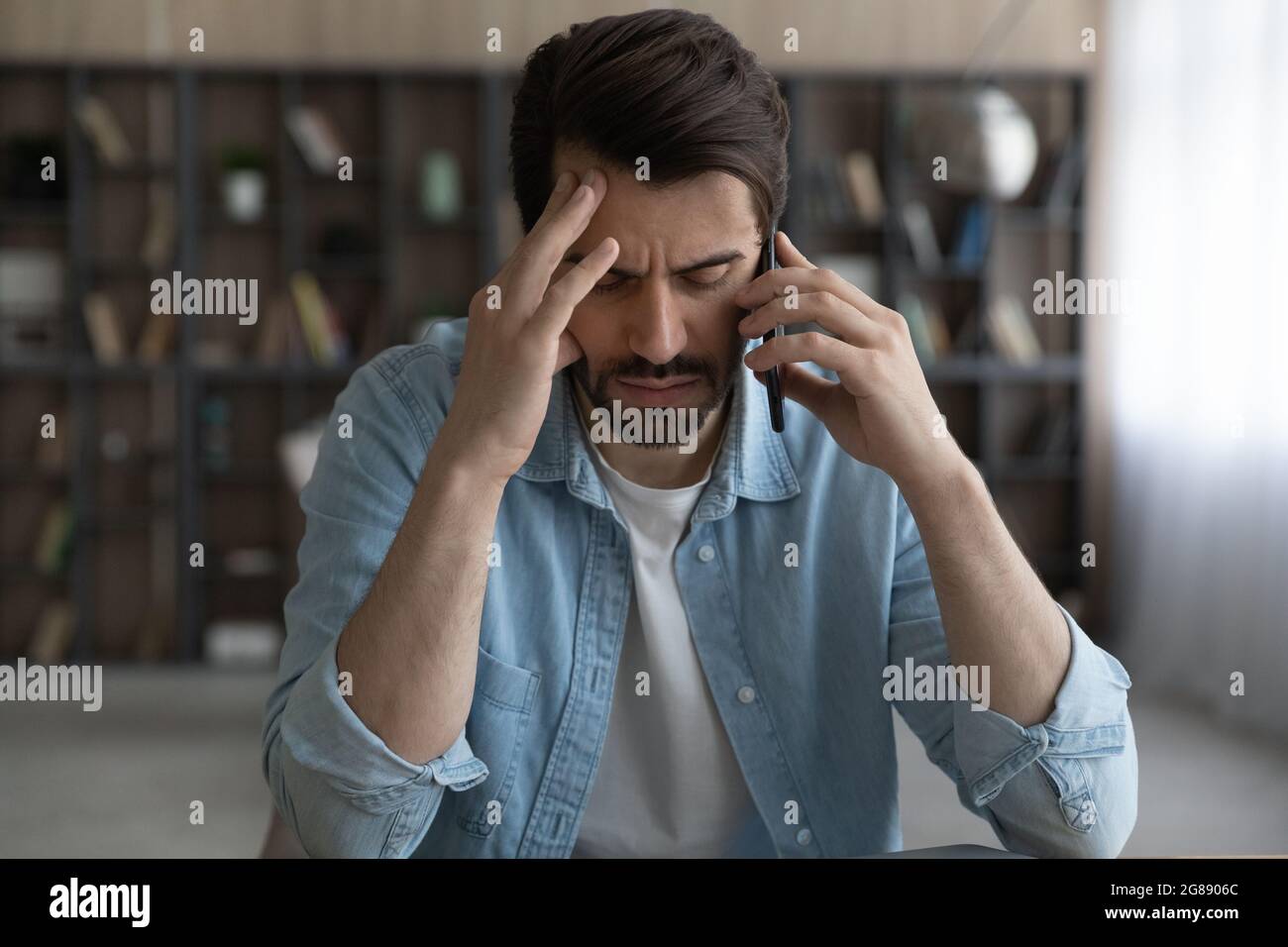 Stressed young man holding cellphone conversation in office. Stock Photo
