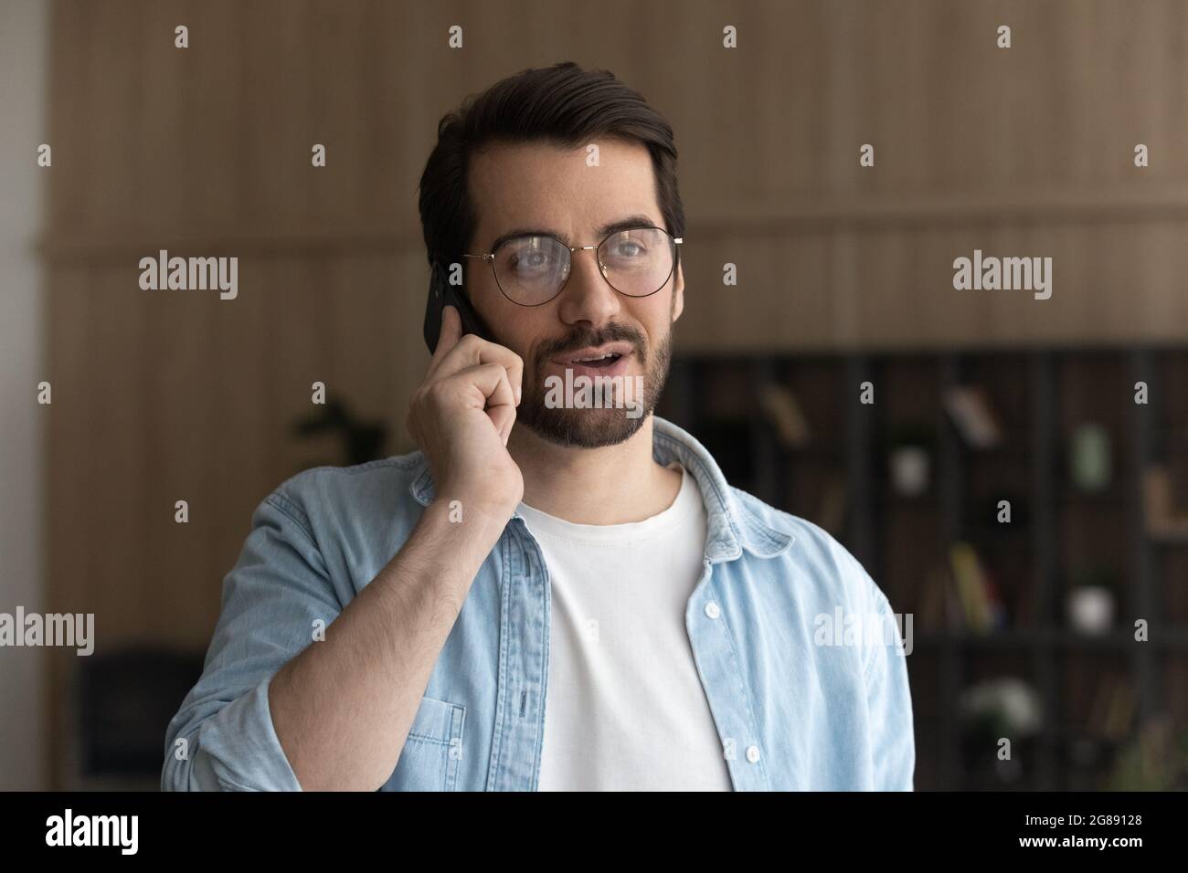 Happy young man in eyeglasses holding cellphone conversation. Stock Photo