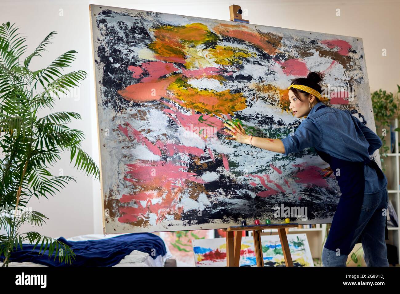 Inspired female artist working on a large modern abstract oil painting, applying paint on canvas