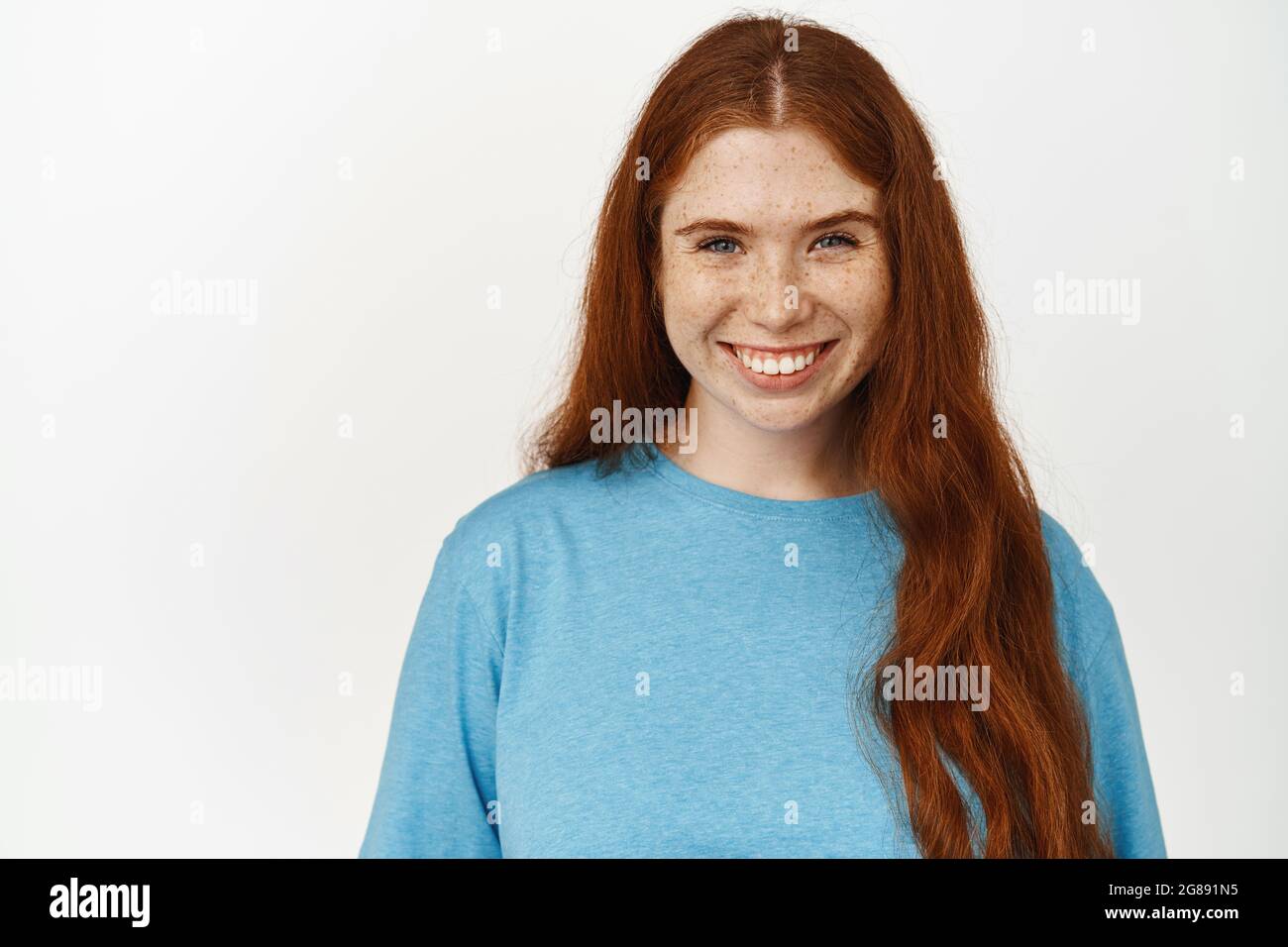 Women beauty. Close up shot of smiling natural girl with long red hair, candid white smile, pale skin and freckles, looking happy at camera, standing Stock Photo
