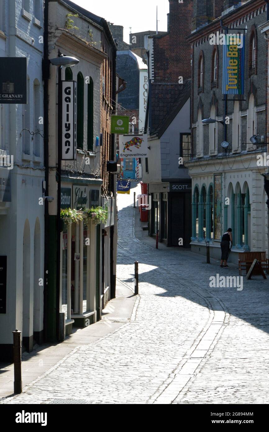 A woman sweeps the pavement in front of her shop in cobbled Bedford Street, Norwich, UK Stock Photo