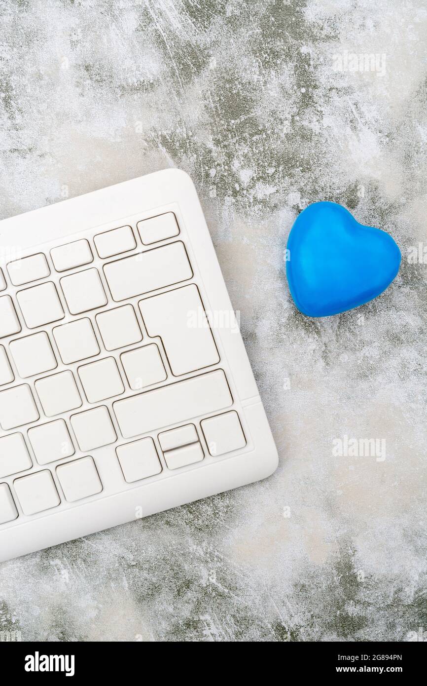 Blue heart + white Qwerty keyboard for Blue Monday, feeling gloomy / dispirited, poor office morale, being dumped online, Covid lockdown mental blues. Stock Photo