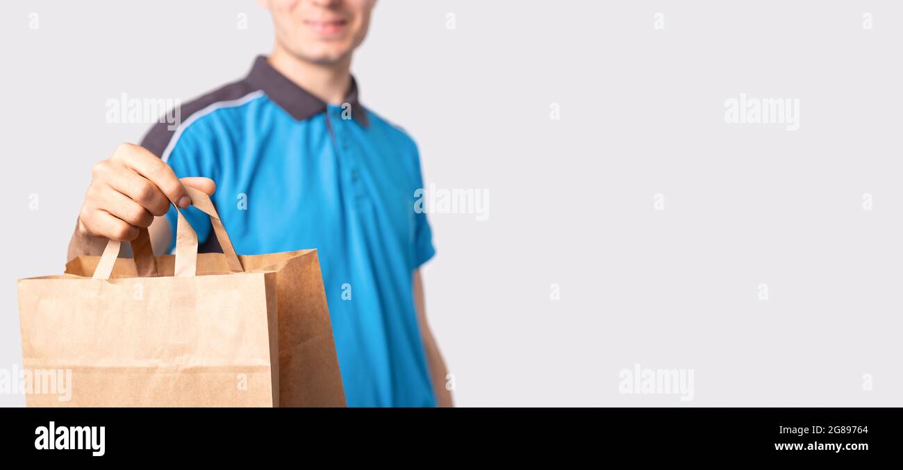 Delivery man in a blue polo shirt holding a package carton bag with handless pulling it forward and smiling. Stock Photo