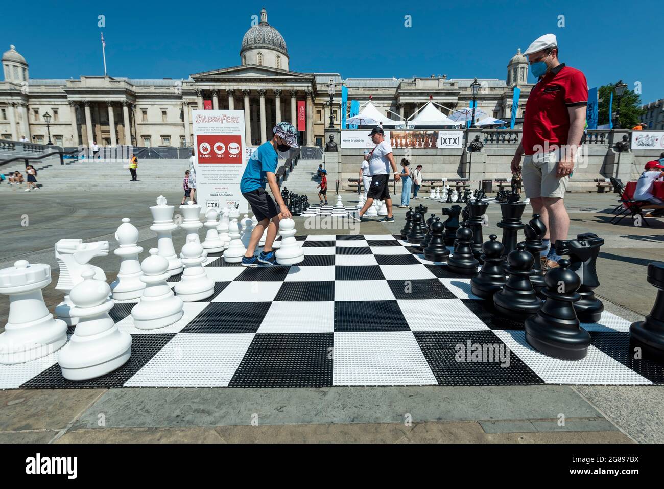 London, UK. 18 July 2021. An outdoor chess game in progress at Chess Fest in  Trafalgar Square. The event celebrates the game of chess and visitors can  learn the game, play chess