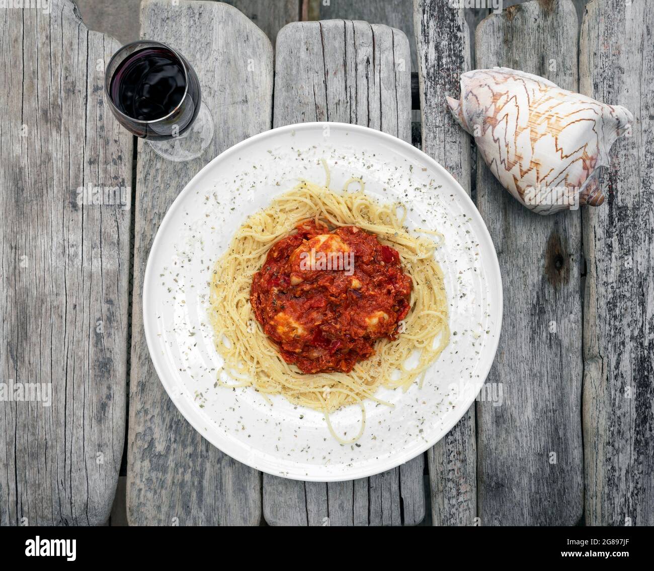 mozzarella bocconcini balls in tomato vegetable ragu sauce with spaghetti on rustic driftwood table with glass of red wine Stock Photo