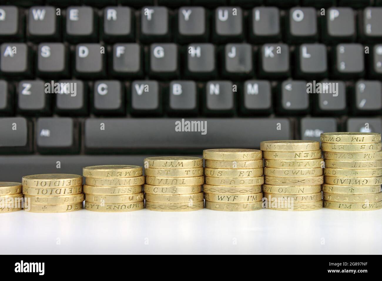 Stacks of coins in a rising column against a backdrop of a computer keyboard. A Metaphor for online transactions. Stock Photo