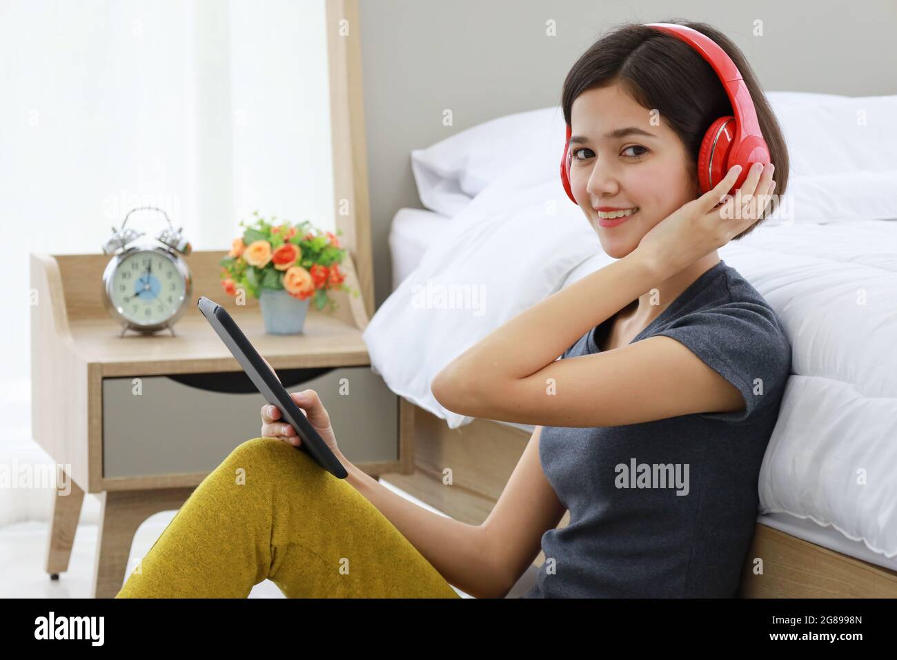 Young and beautiful half raced Thai-German girl wearing red headphone listening to music and using tablet computer in house bedroom. Idea for lifestyl Stock Photo