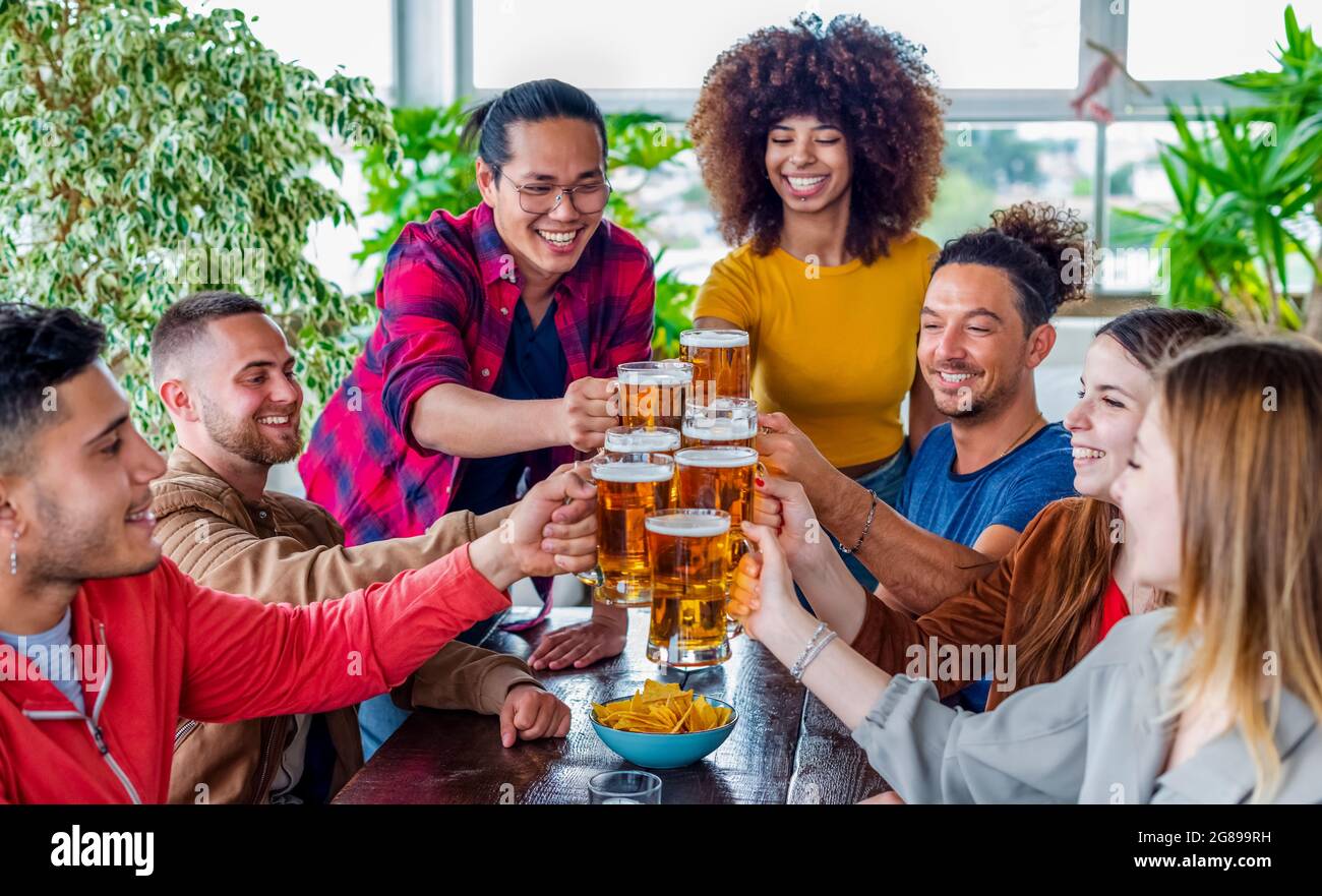 diverse group of friends celebrating happy hour making a toast with pint glasses of beers inside a bar restaurant. multiethnic people together in pub Stock Photo