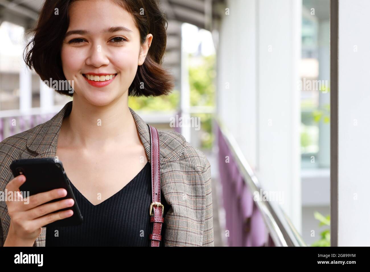 Close up shot on cute wide-open smile face of young and beautiful Asian businesswoman in casual business suit holding smartphone and looking at camera Stock Photo
