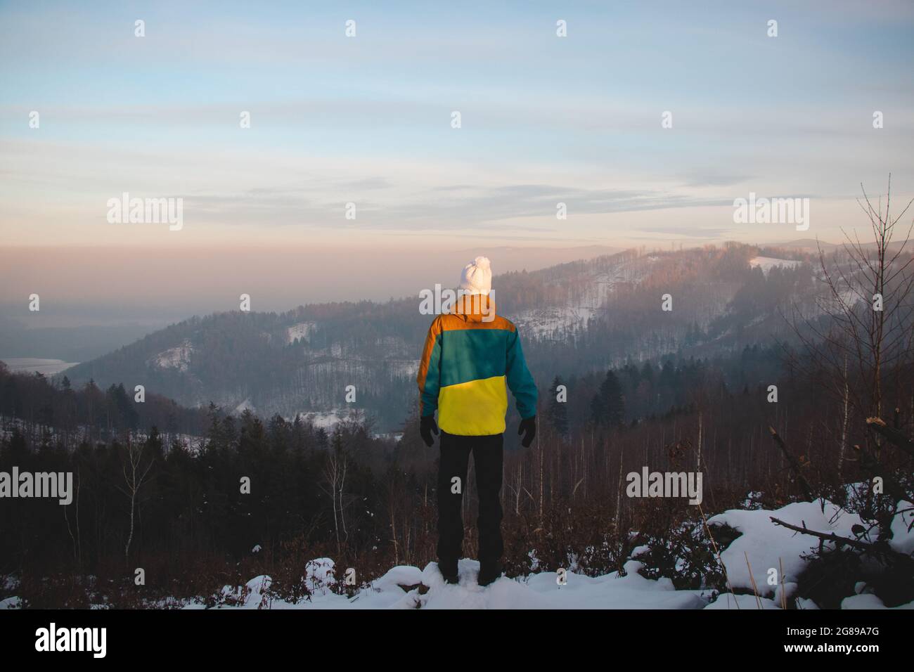 Climbing a mountain in the Alps and enjoying the view of a valley in the Austrian Western Alps. A young boy aged 15-20 in winter clothes standing on t Stock Photo