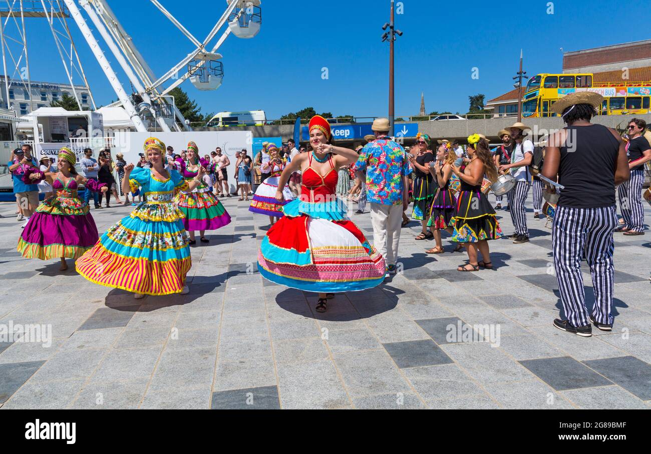 Bournemouth, Dorset, UK. 18th July, 2021. Afon Sistema with their whirling dancers with colourful skirts play Maracatu, Samba's earthier cousin from Northeastern Brazilas perform as part of the Arts by the Sea Summer Series on a hot sunny crowded day at the seaside. Credit: Carolyn Jenkins/Alamy Live News Stock Photo