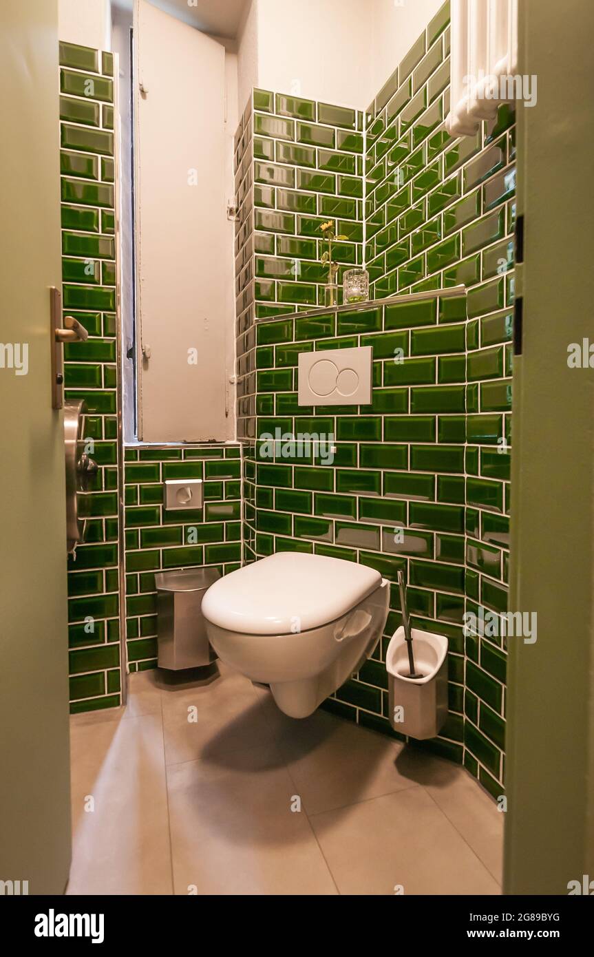 Glance into an extraordinary guest toilet. with wall-hung toilet, which was attached over a corner. The small dark green tiles are particularly notice Stock Photo