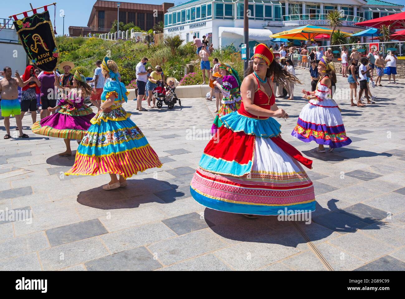 Bournemouth, Dorset, UK. 18th July, 2021. Afon Sistema with their whirling dancers with colourful skirts play Maracatu, Samba's earthier cousin from Northeastern Brazilas perform as part of the Arts by the Sea Summer Series on a hot sunny crowded day at the seaside. Credit: Carolyn Jenkins/Alamy Live News Stock Photo