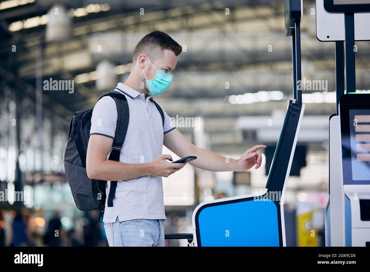 Man using self service check-in machine. Passenger scanning ticket on smart phone at airport terminal. Stock Photo