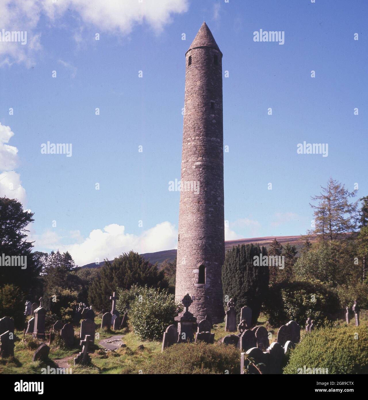 1960s, historical view from this era of The Round Tower standing in a graveyard at a cemetery at the ancient monastic site of Glendalough at Wicklow, Ireland. The most famous of all the landmarks in Glendalough, the Round Tower is 33 metres high and was built around 1000 years ago by the monks of St. Kevin’s monastery. Stock Photo