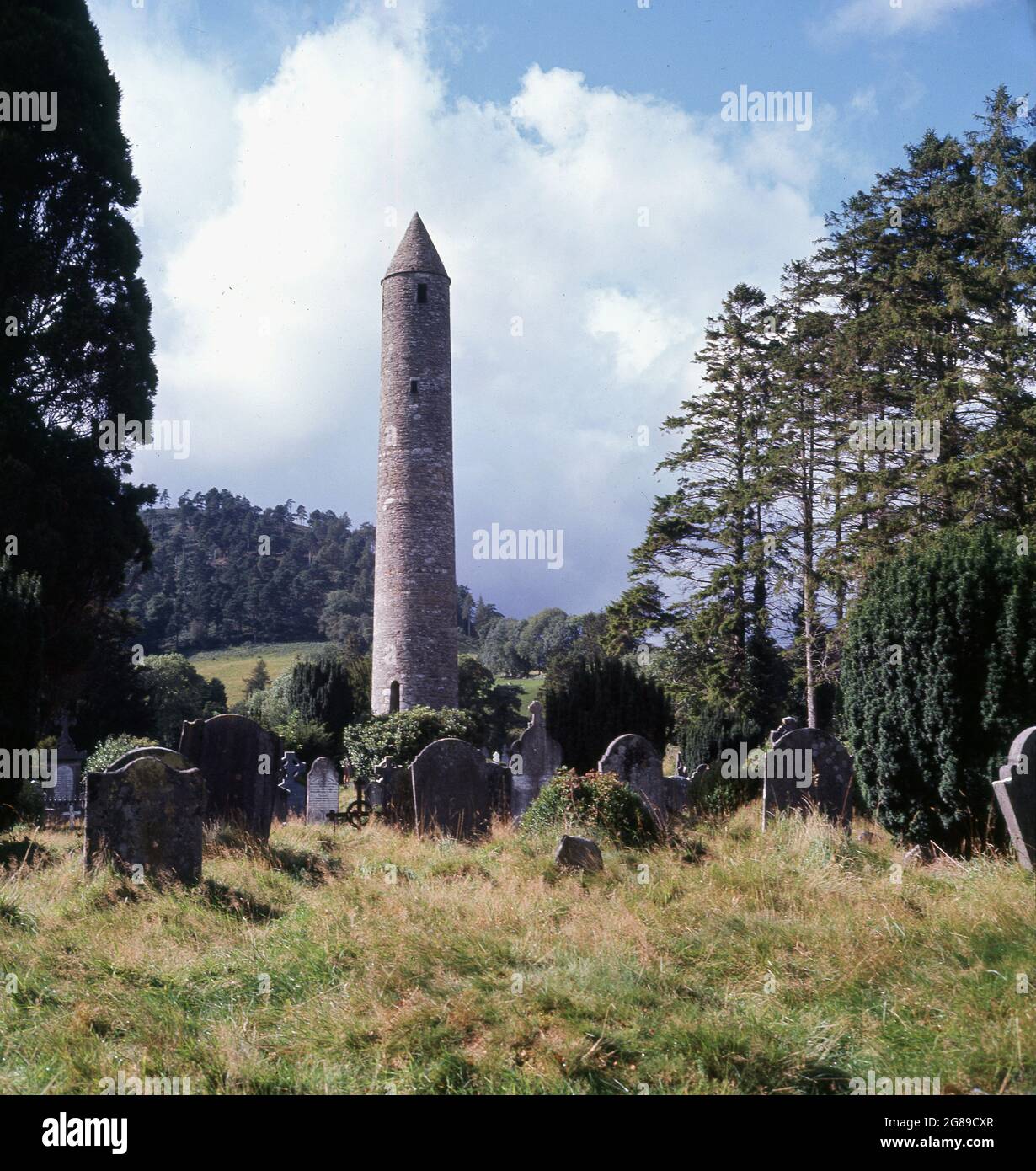 1960s, historical view from this era of The Round Tower standing in a graveyard at a cemetery at the ancient monastic site of Glendalough at Wicklow, Ireland. The most famous of all the landmarks in Glendalough, the Round Tower is 33 metres high and was built around 1000 years ago by the monks of St. Kevin’s monastery. Stock Photo