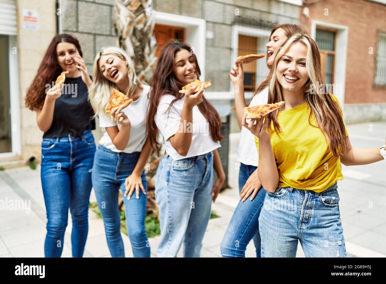 Group of young woman friends smiling happy eating pizza standing at the ...