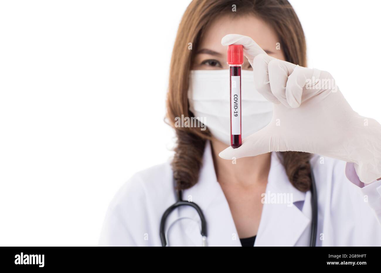 Pretty beautiful Asian woman in doctor gown or lab coat wearing surgical hygiene mask holding and analyzing test tube of Covid-19 sample. Idea for try Stock Photo