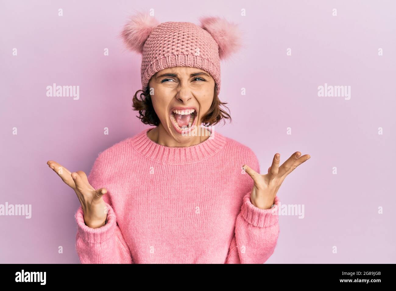 Young brunette woman wearing cute wool cap crazy and mad shouting and yelling with aggressive expression and arms raised. frustration concept. Stock Photo