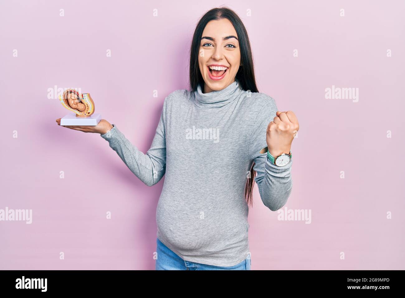 Beautiful woman with blue eyes expecting a baby, holding anatomic fetus ...