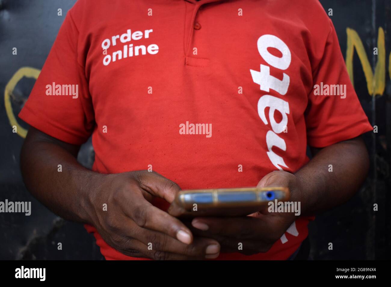 Kolkata, India. 17th July, 2021. A delivery worker of Zomato, an Indian food-delivery start-up check his phone and wait to collect orders outside a restaurant in Kolkata. (Photo by Sudipta Das/Pacific Press/Sipa USA) Credit: Sipa USA/Alamy Live News Stock Photo