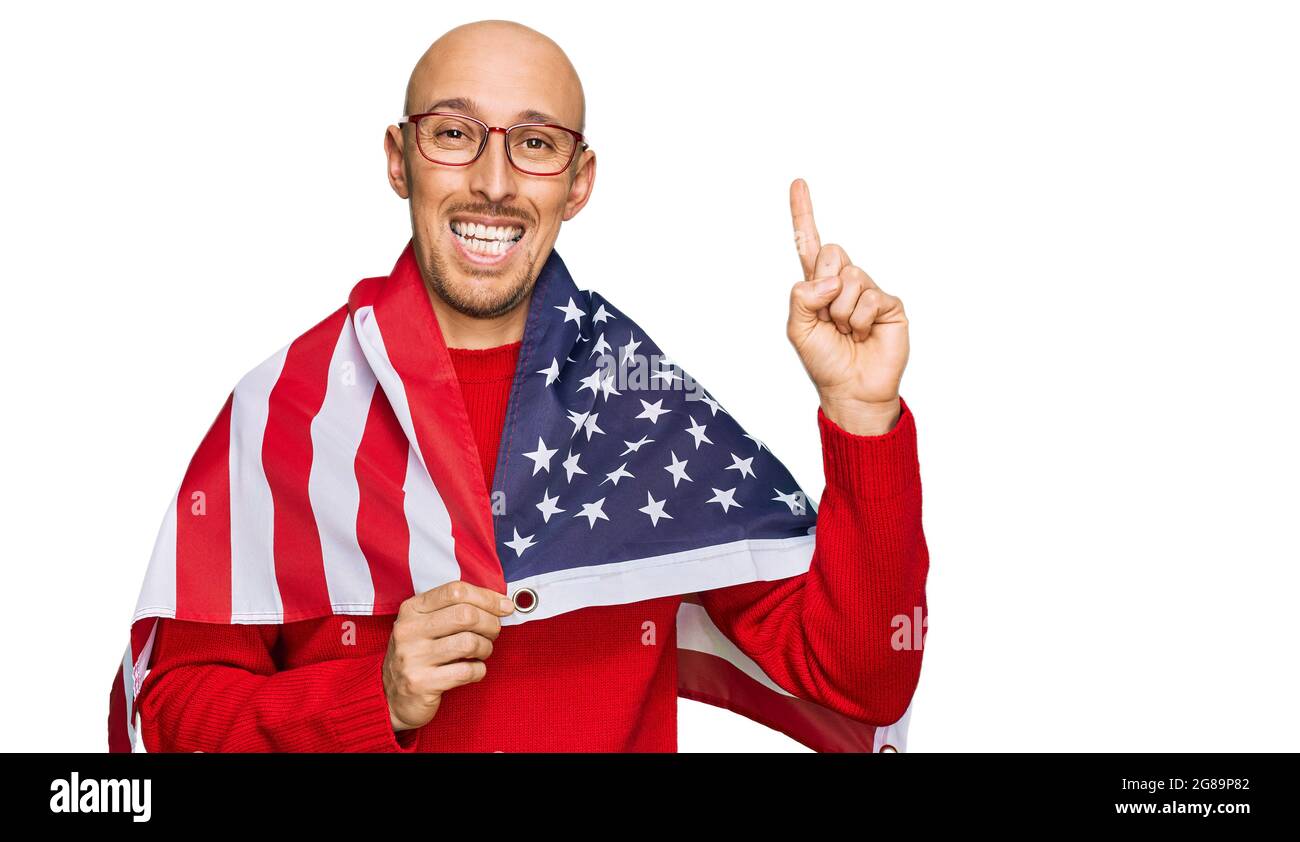 Bald man with beard wrapped around united states flag surprised with an idea or question pointing finger with happy face, number one Stock Photo