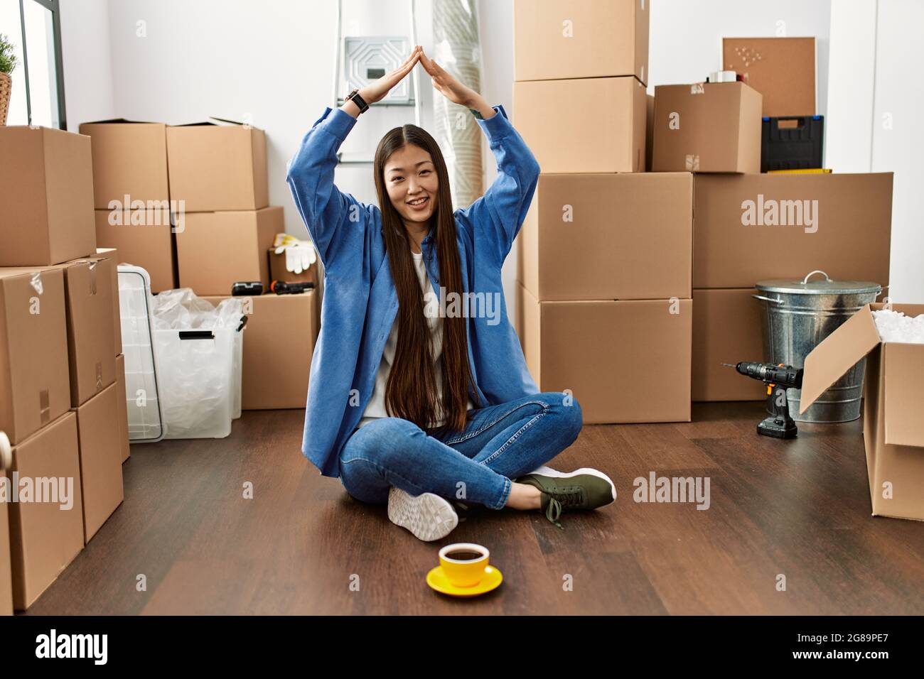 Young chinese girl smiling happy doing house gesture with hands raised ...