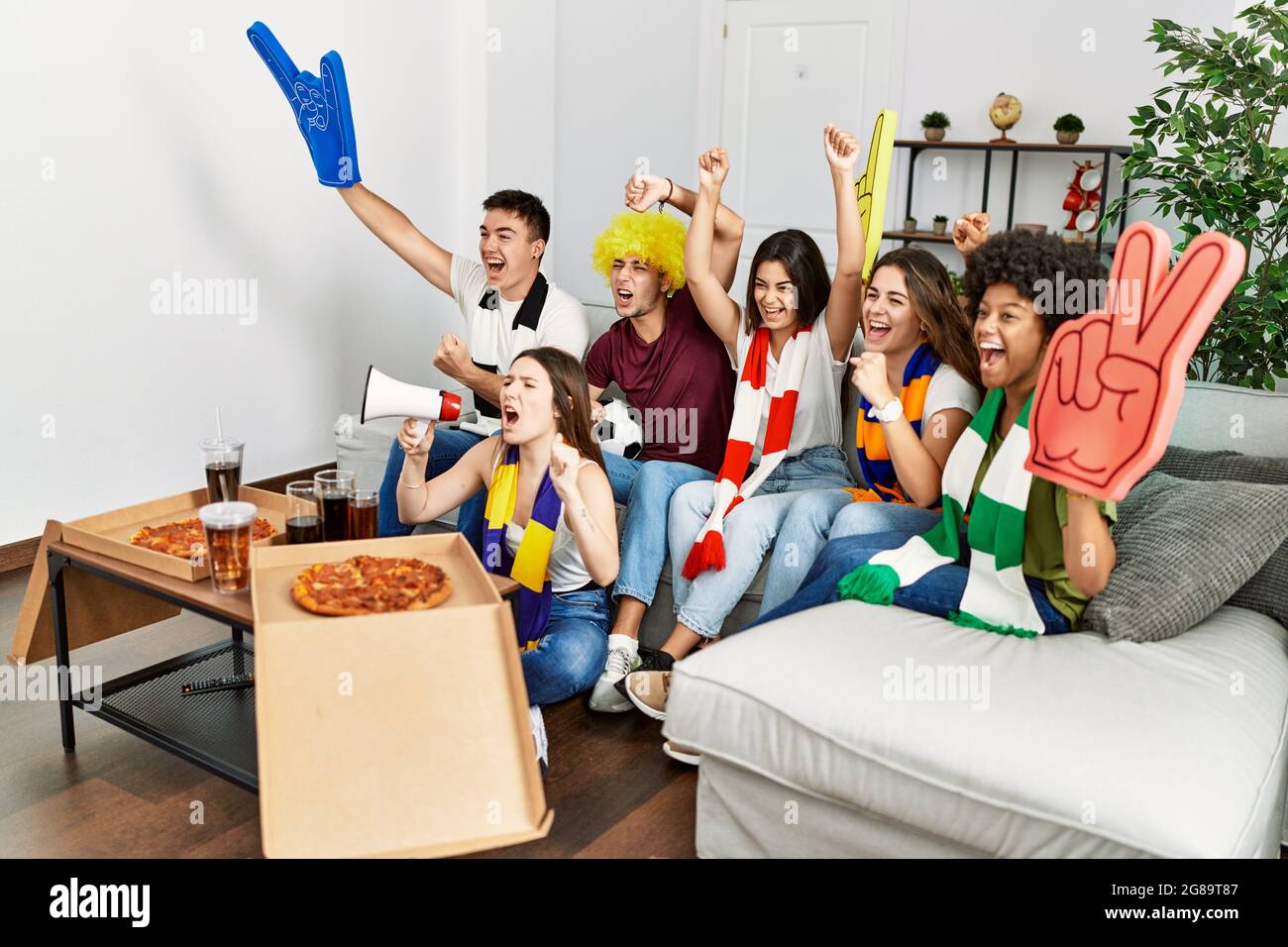 Group of young friends watching and supporting soccer match eating ...