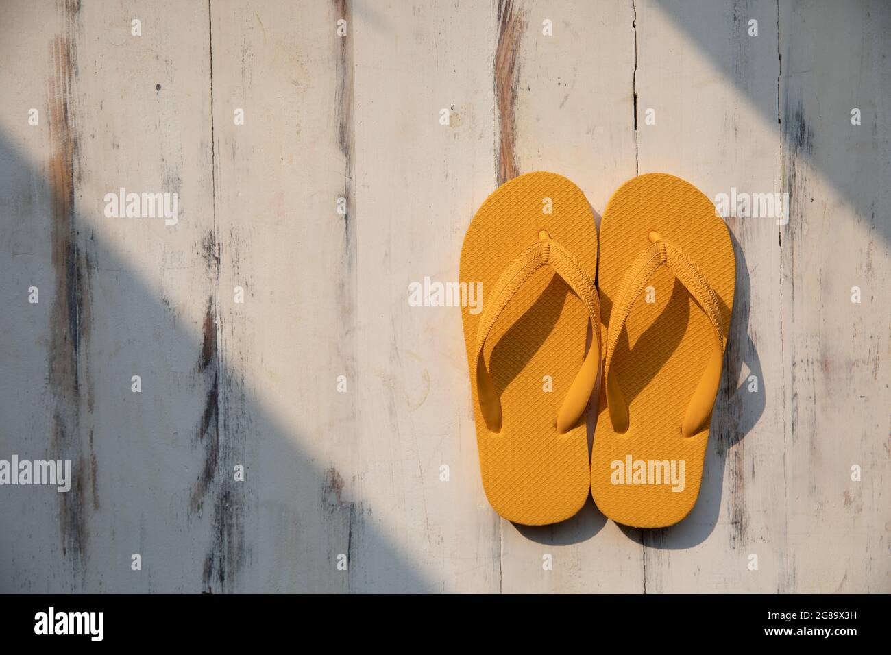 A of colorful yellow rubber slippers popular use on a sand beach and tropical tourist destinations such as island on wood background with sunligh Stock Photo - Alamy