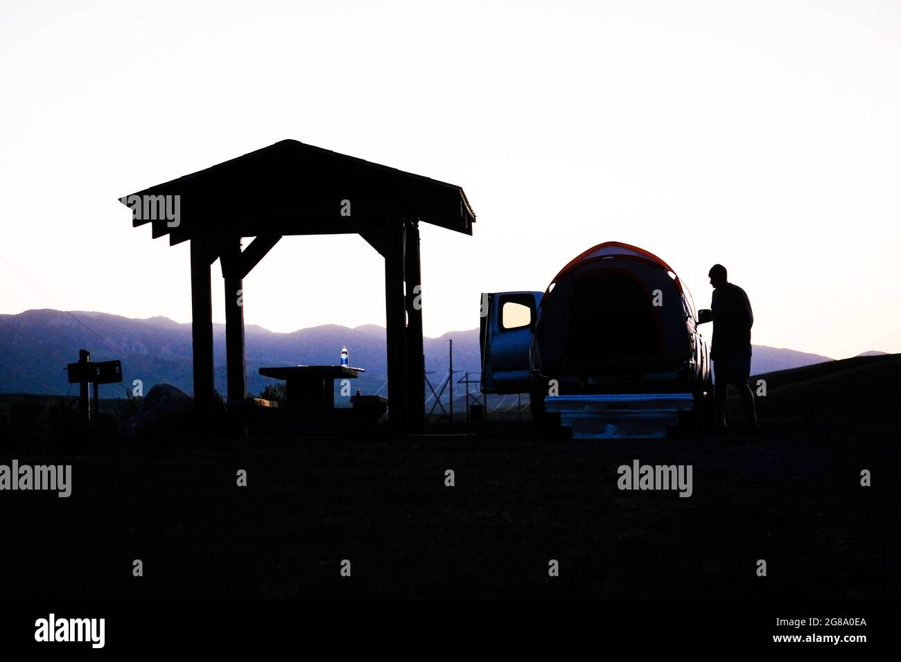 Camper is silhouetted next to a pickup truck with tent at DeSmet Lake Campground near Buffalo, Wyoming, USA. Stock Photo