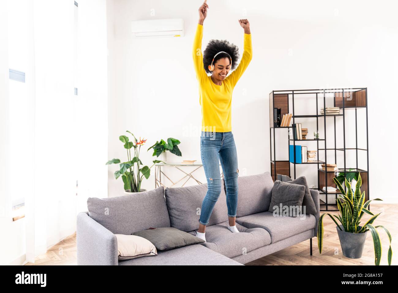 Happy woman listening music, jumping and dancing on the sofa at home ...