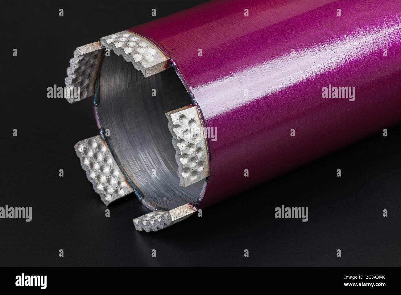 Modern core drill bit in beautiful detail on a black background. Purple water cooled hole saw cutter with sharp crown of diamond grit alloy segments. Stock Photo