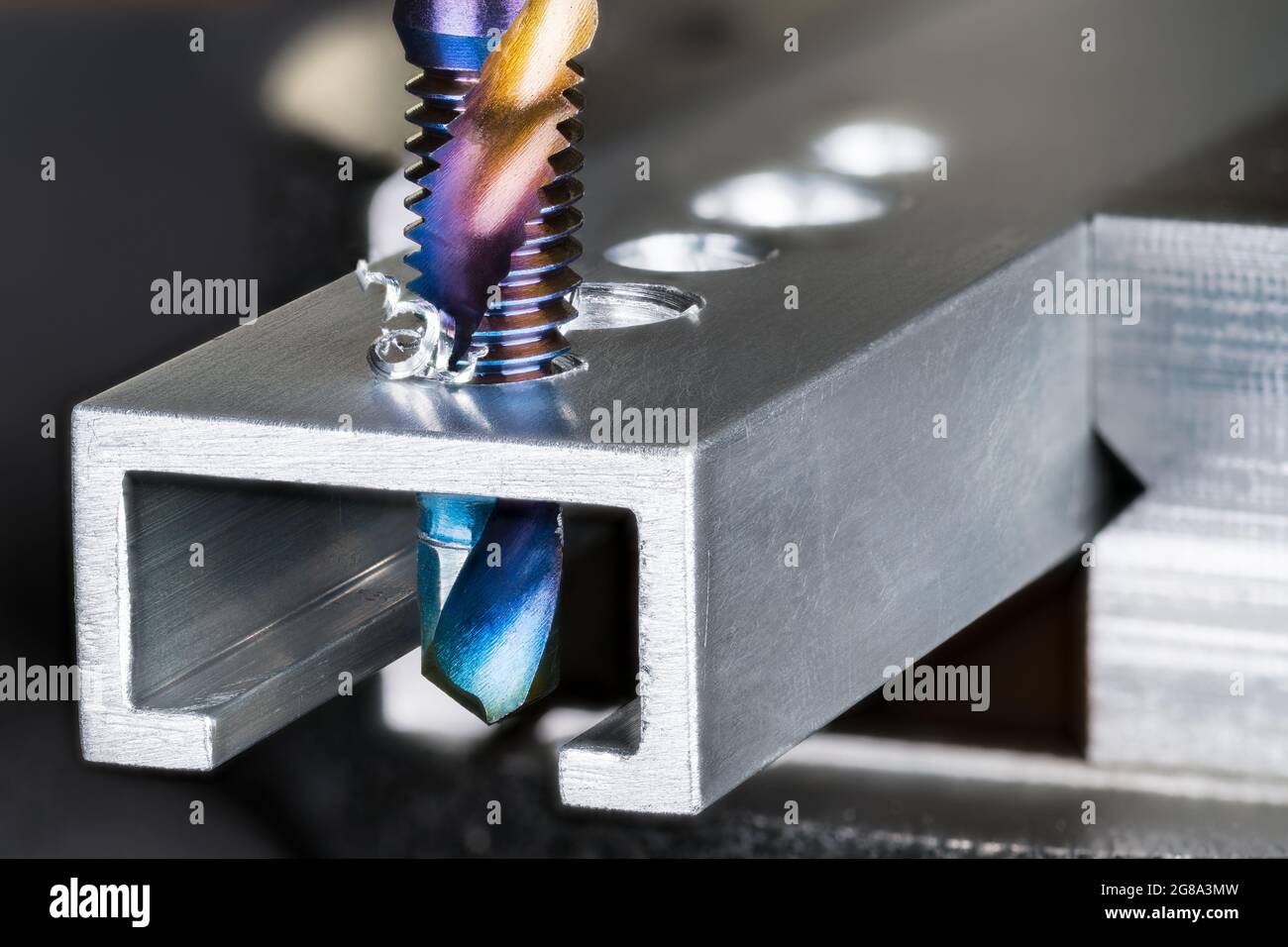 Closeup of tap and drill bit making a threaded hole in an aluminum profile with metal shavings. Professional drilling and tapping tool. Chip machining. Stock Photo