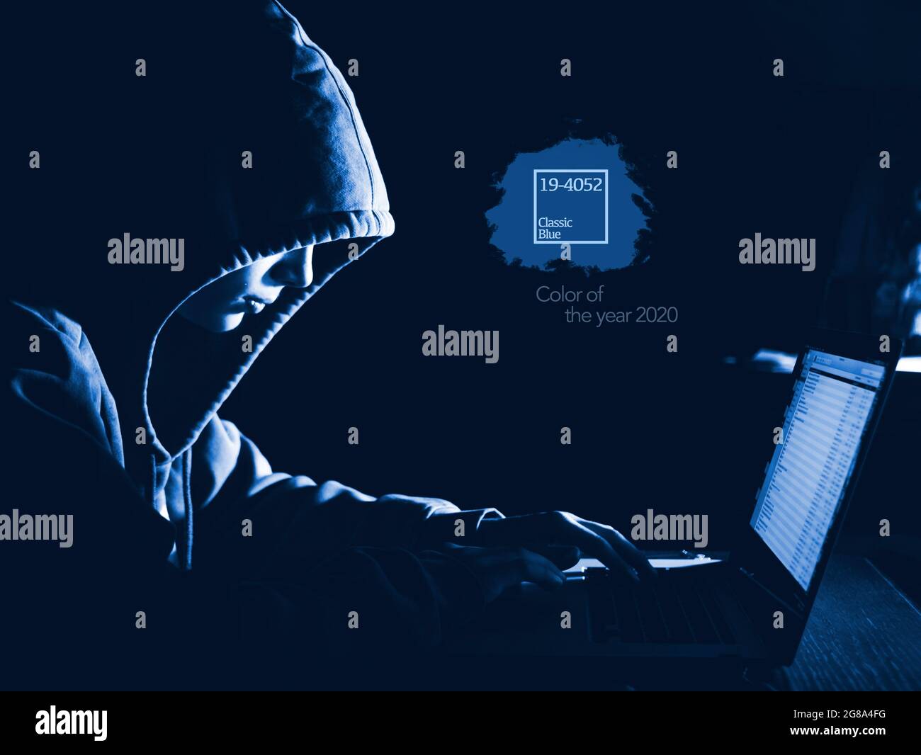 anonimous man in the hoodie in dark studio typing text online , color of the 2020 year trend, classic blue tones Stock Photo