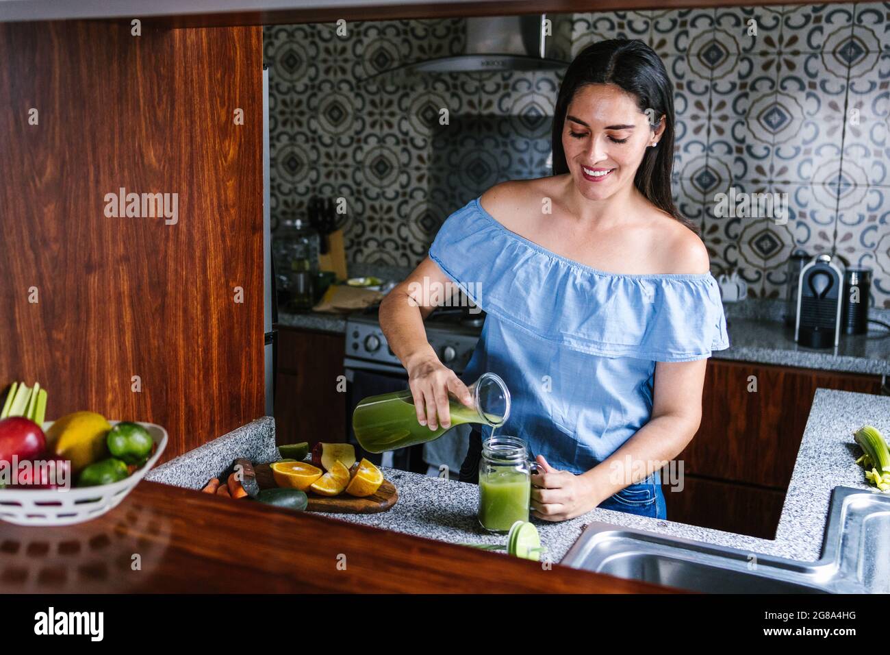 Latin Woman making green smoothie or Detox juice in kitchen at Home in healthy eating concept in Mexico Stock Photo