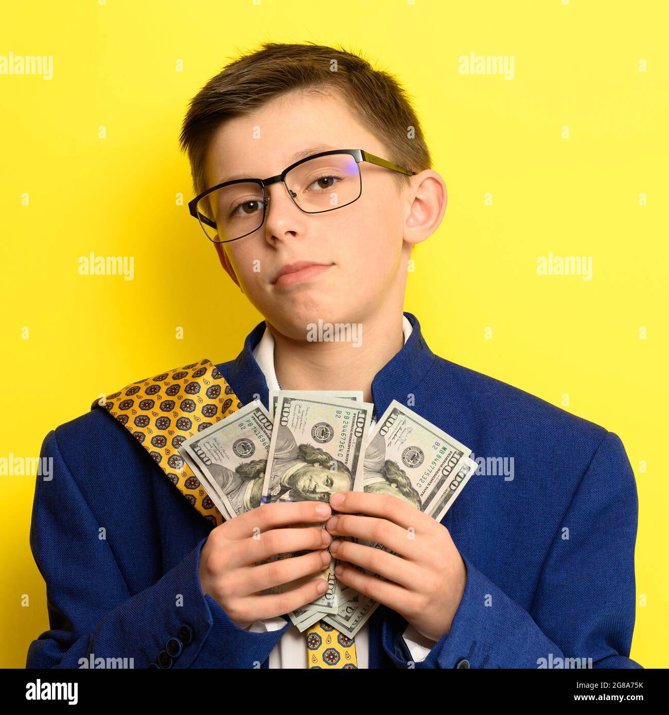 A boy in glasses and an oversized suit with a satisfied face is holding