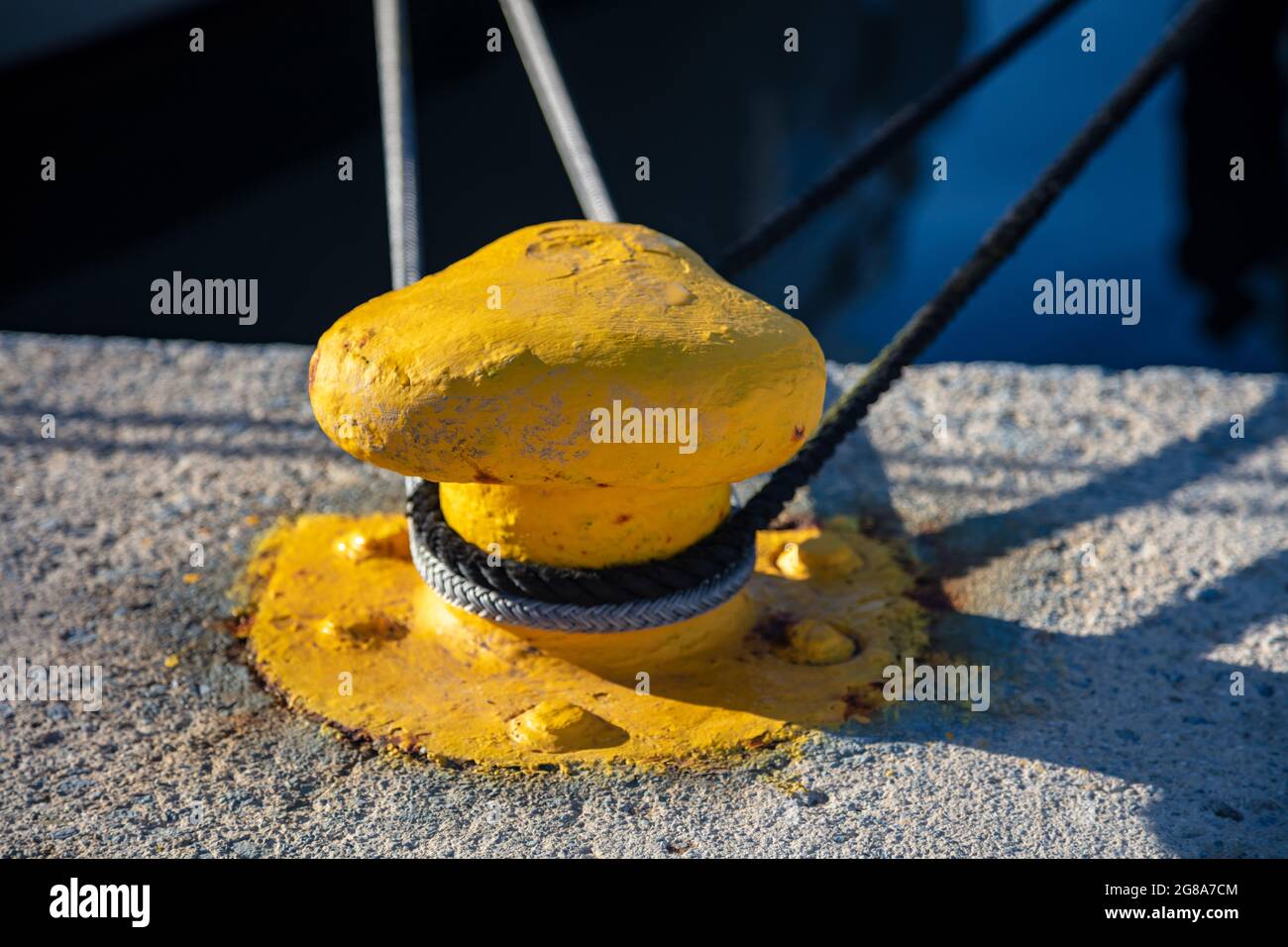 Mooring bollard concept. Ropes twisted with knobs on yellow metal steel bollard. Secured moored yachts at harbor marina quay, Greece. Close up, sunny Stock Photo
